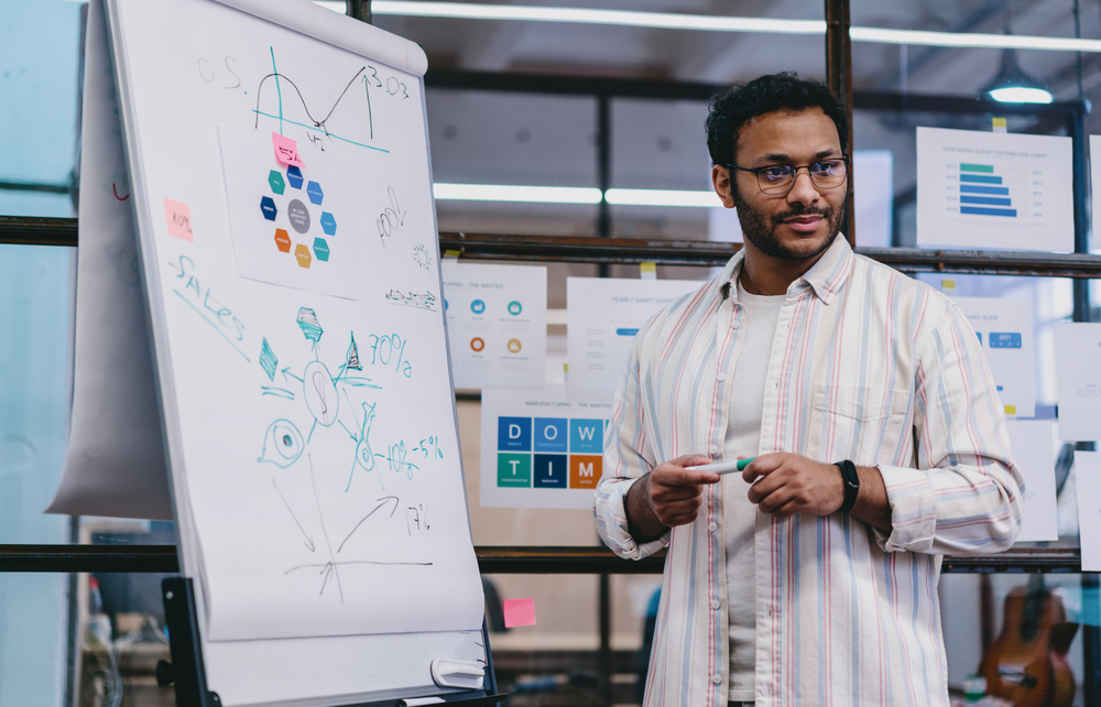 cheerful ethnic man standing in office by charts a VYJETGT